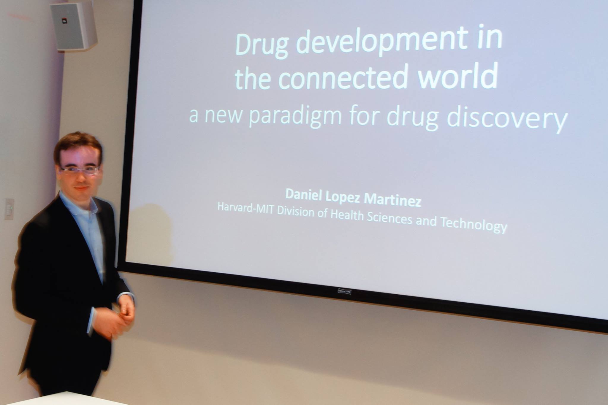 Daniel Lopez-Martinez presenting on drug development in the connected world at the MIT Media Lab Industry Symposium, with the presentation slide visible behind him.