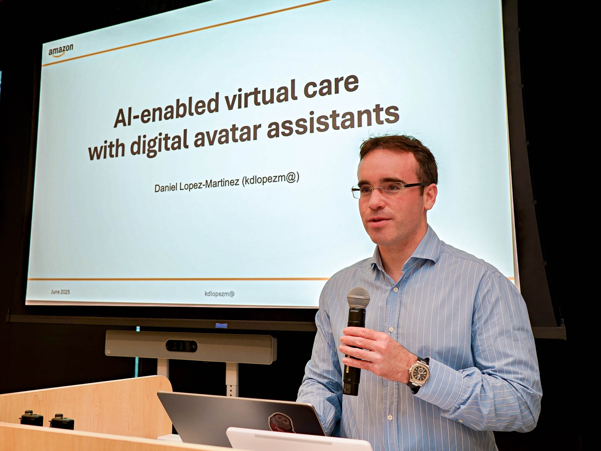 Daniel Lopez-Martinez presenting his talk on AI-enabled virtual care with LLM-powered digital avatar assistants at the Amazon AWS Image and Video Generation Workshop 2025 in Seattle. The title slide behind him shows his name and the Amazon logo.